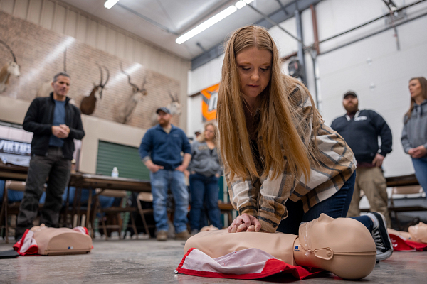 woman preforming CPR on a test dummy with 4 people watching in the background